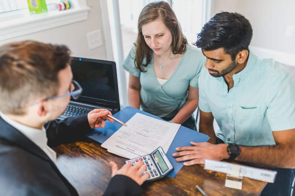 Un conseiller en gestion de patrimoine discute avec un couple de dirigeants, analysant des documents financiers et patrimoniaux pour planifier leur succession et optimiser leur fiscalité